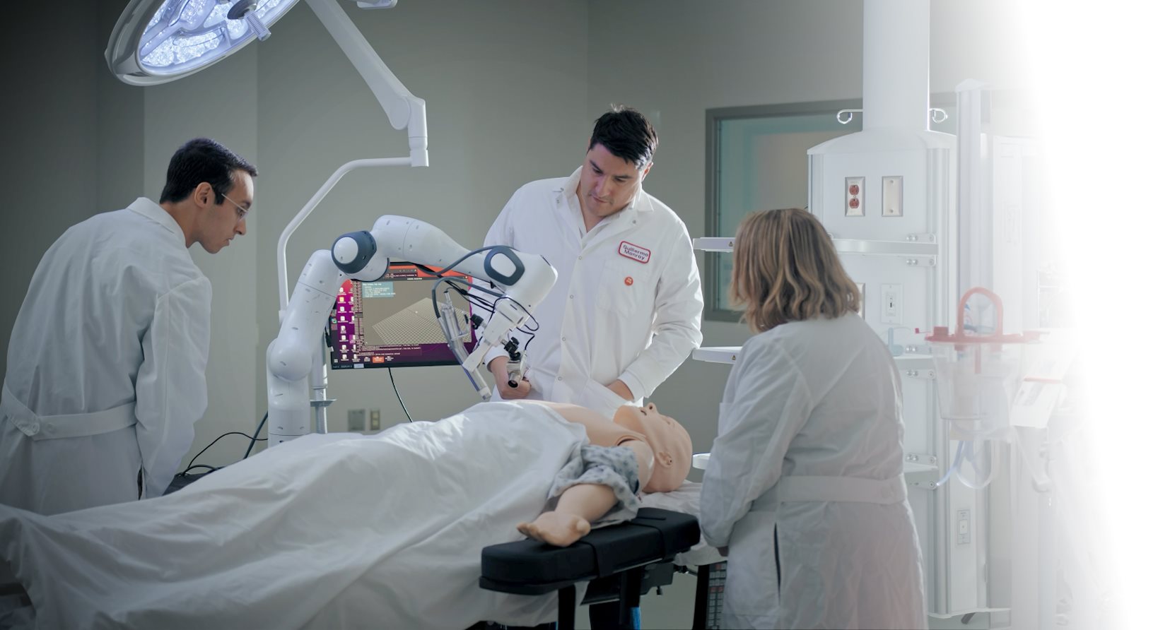 operating room with surgical robot arm, simulated patient, and three people in lab coats