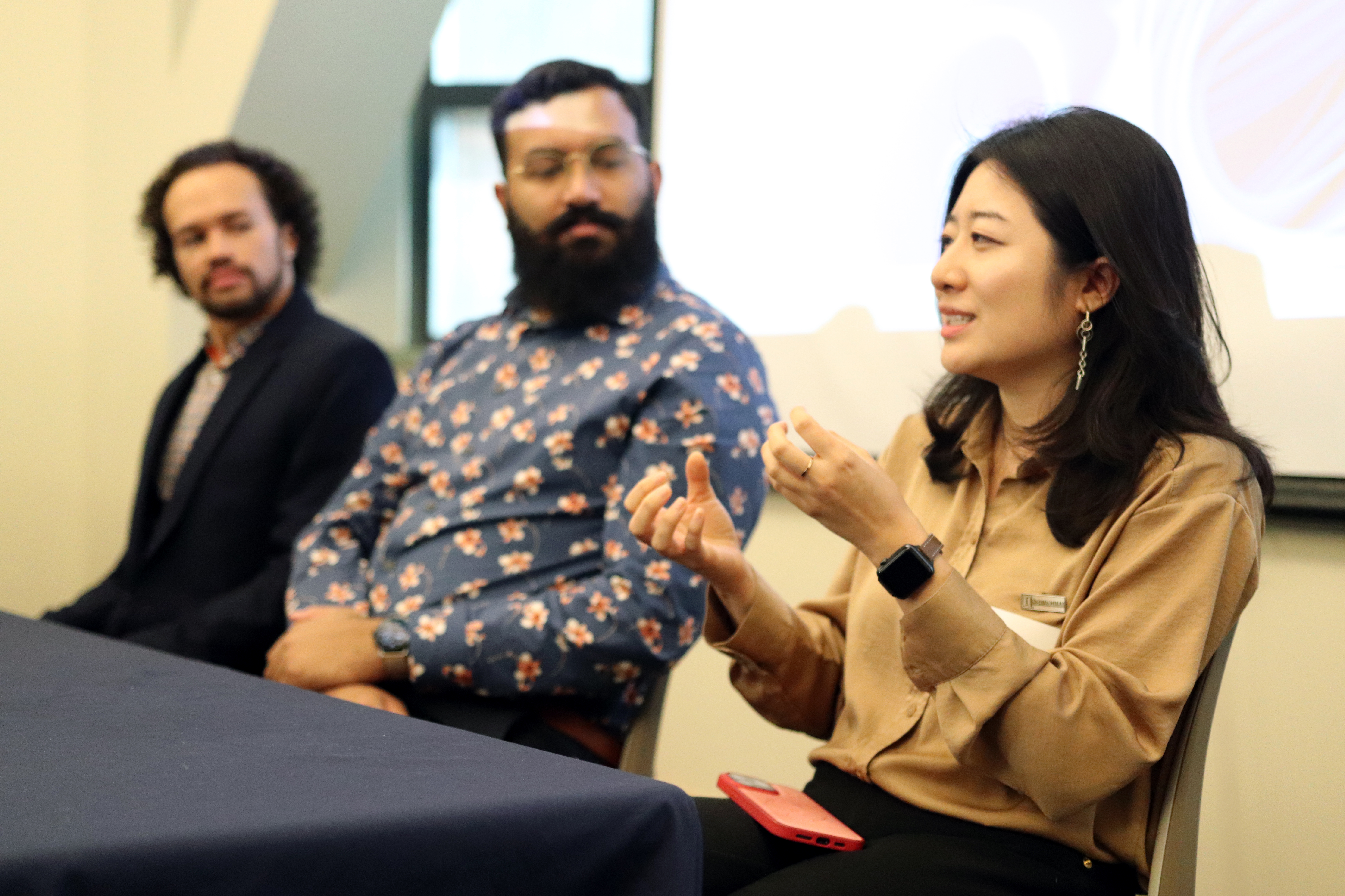 Zhan answers a question seated behind a table while Vaidyam and Wallace listen