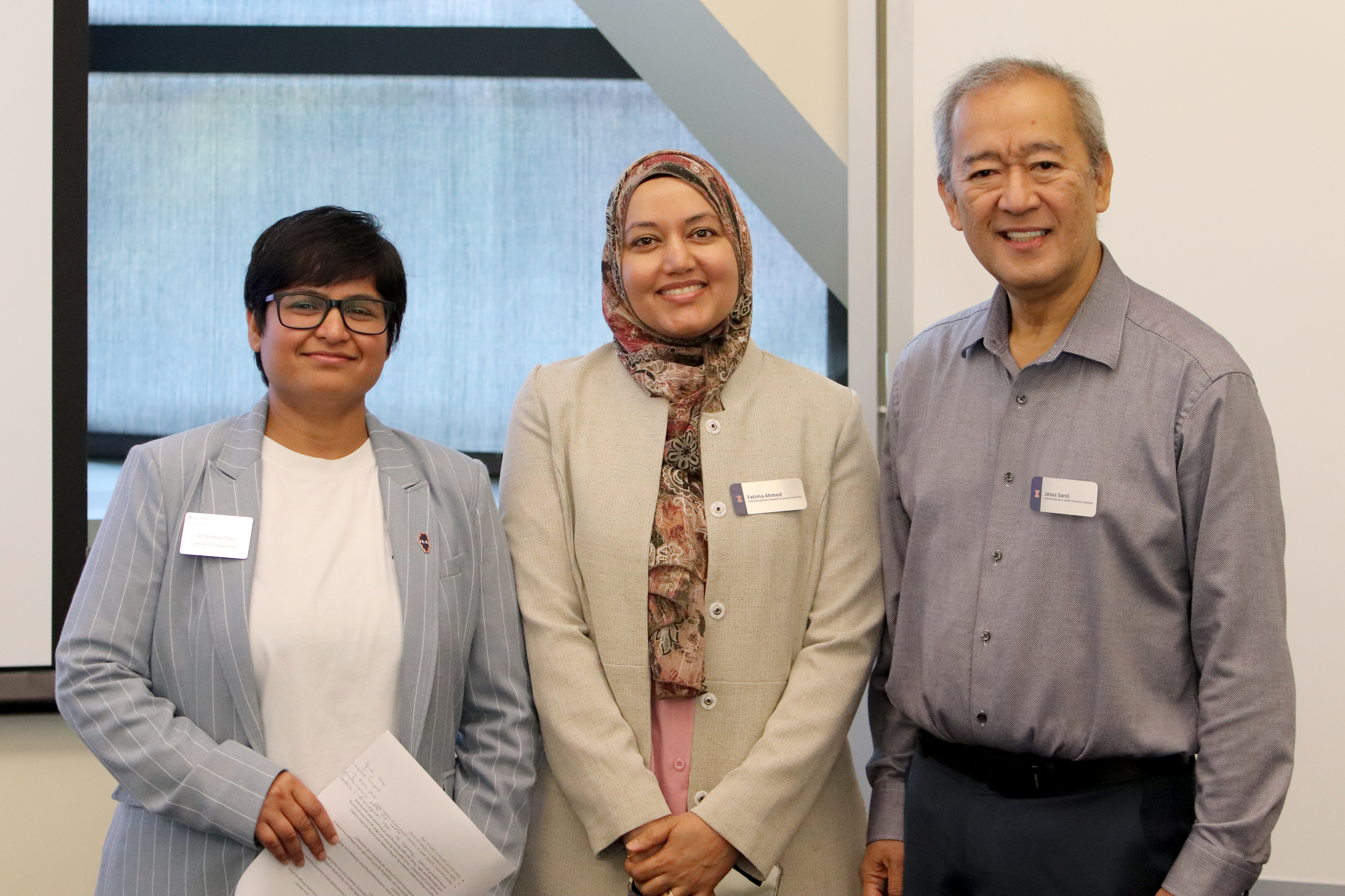 Kaur, Ahmed, and Sarol stand together in front of window