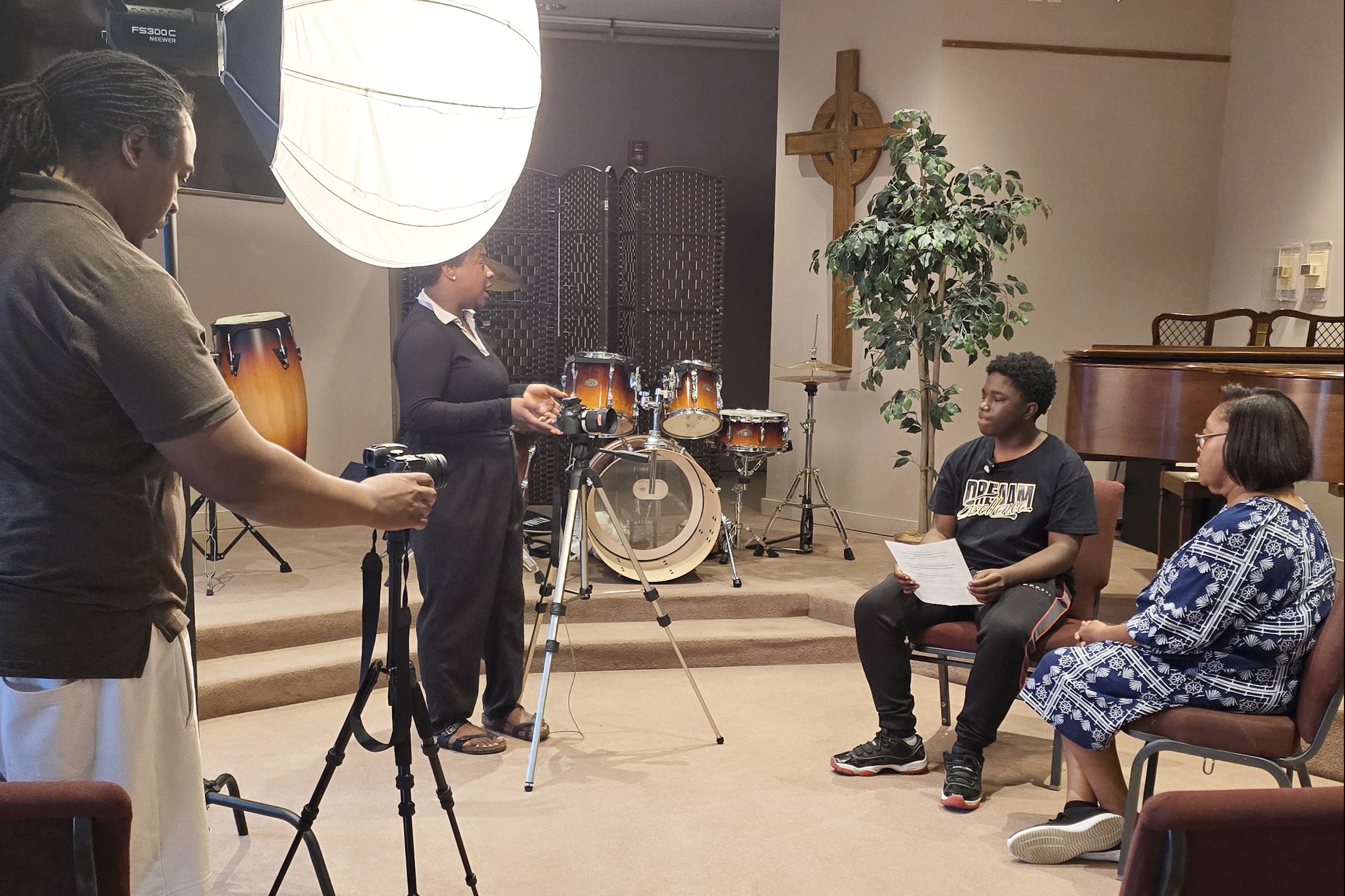 a behind-the-scenes angle showing two videographers standing with cameras and lights preparing two seated interviewees