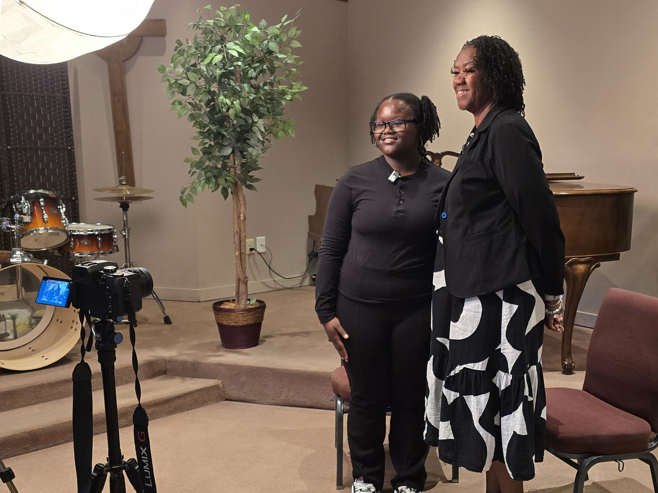 a teenage girl and middle-aged woman pose together for a photo being taken out of the frame with a camera and umbrella light in the foreground