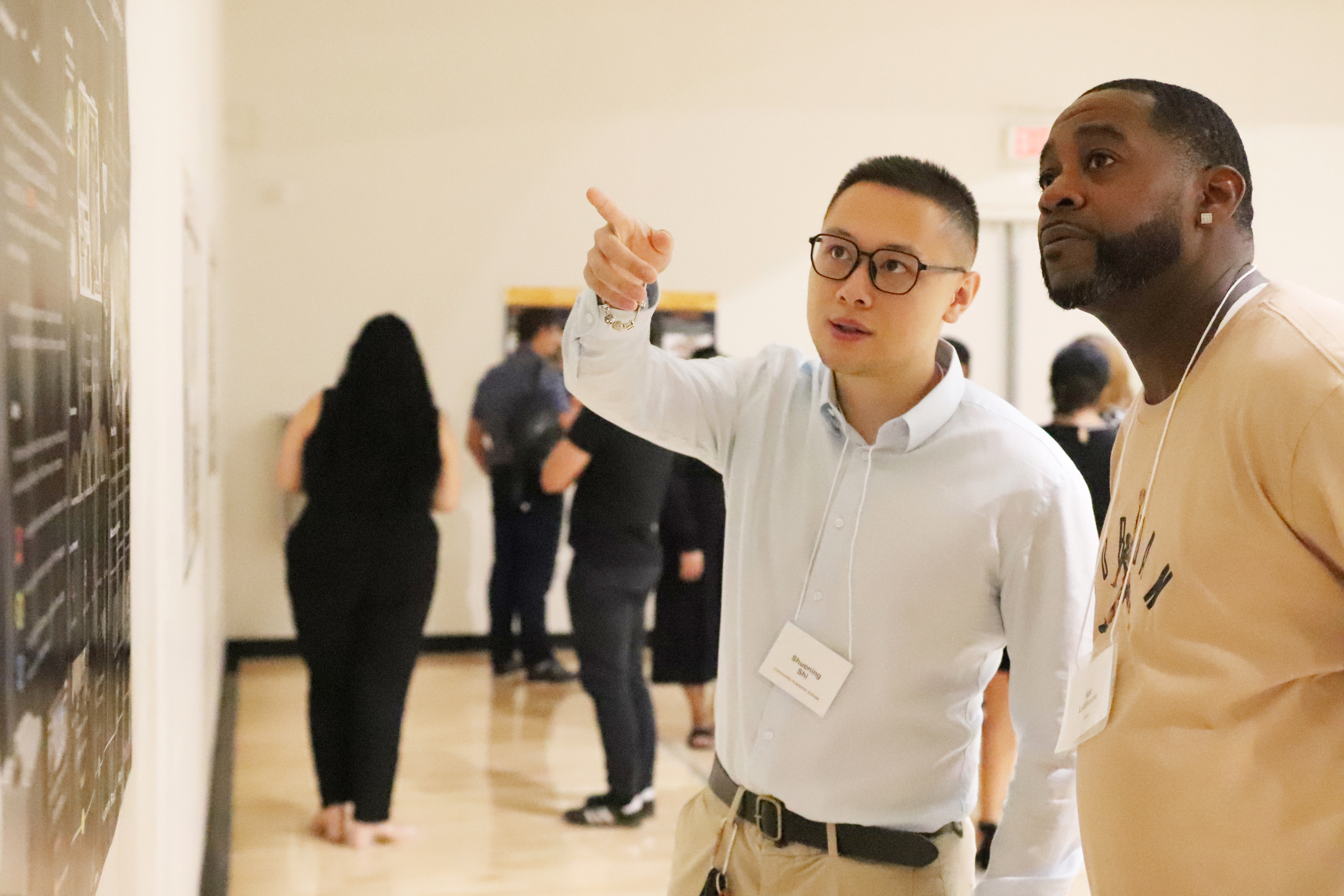 student scholar points to his poster while presenting to an onlooker