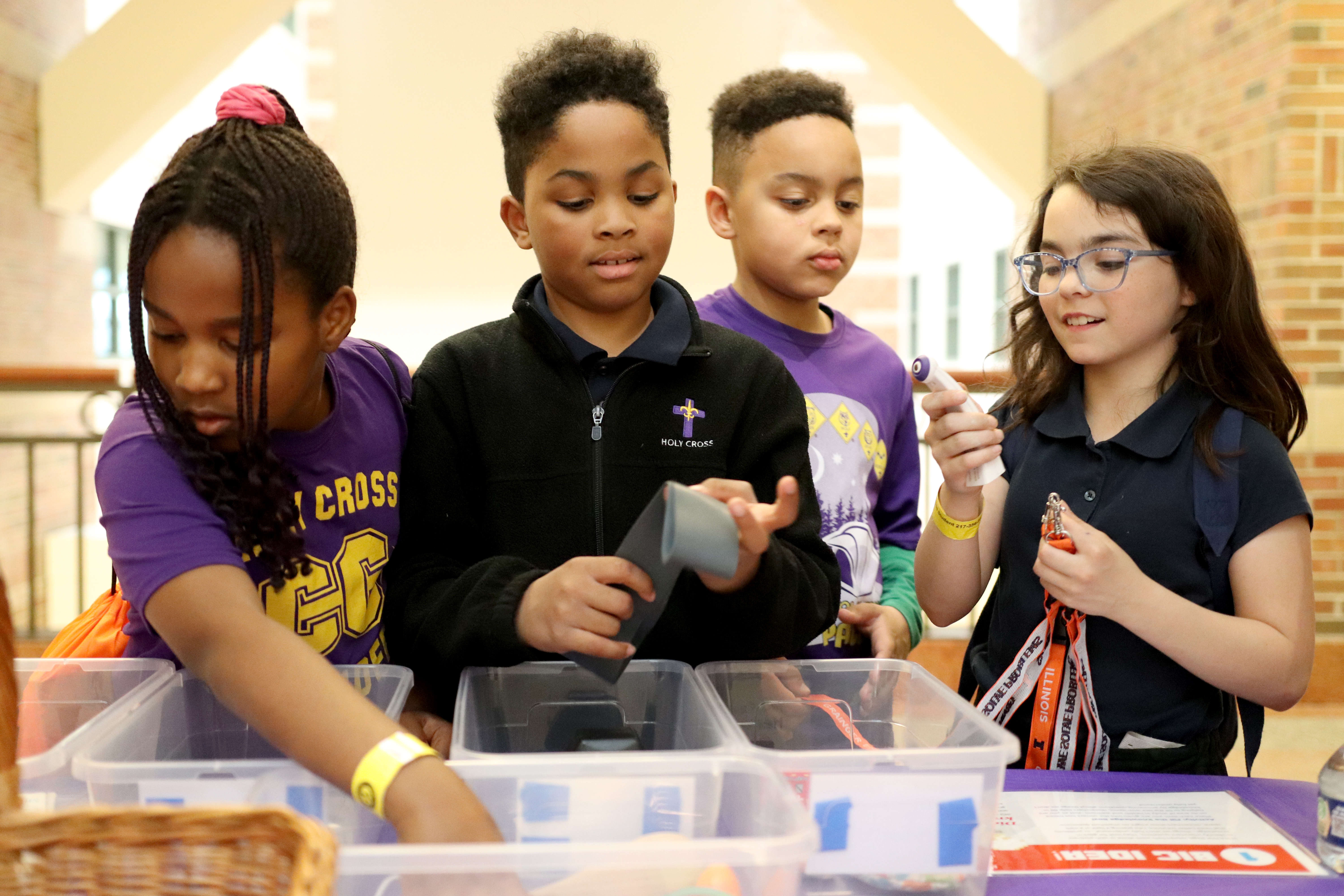 Four kids stand at table while sorting items into clear bins.