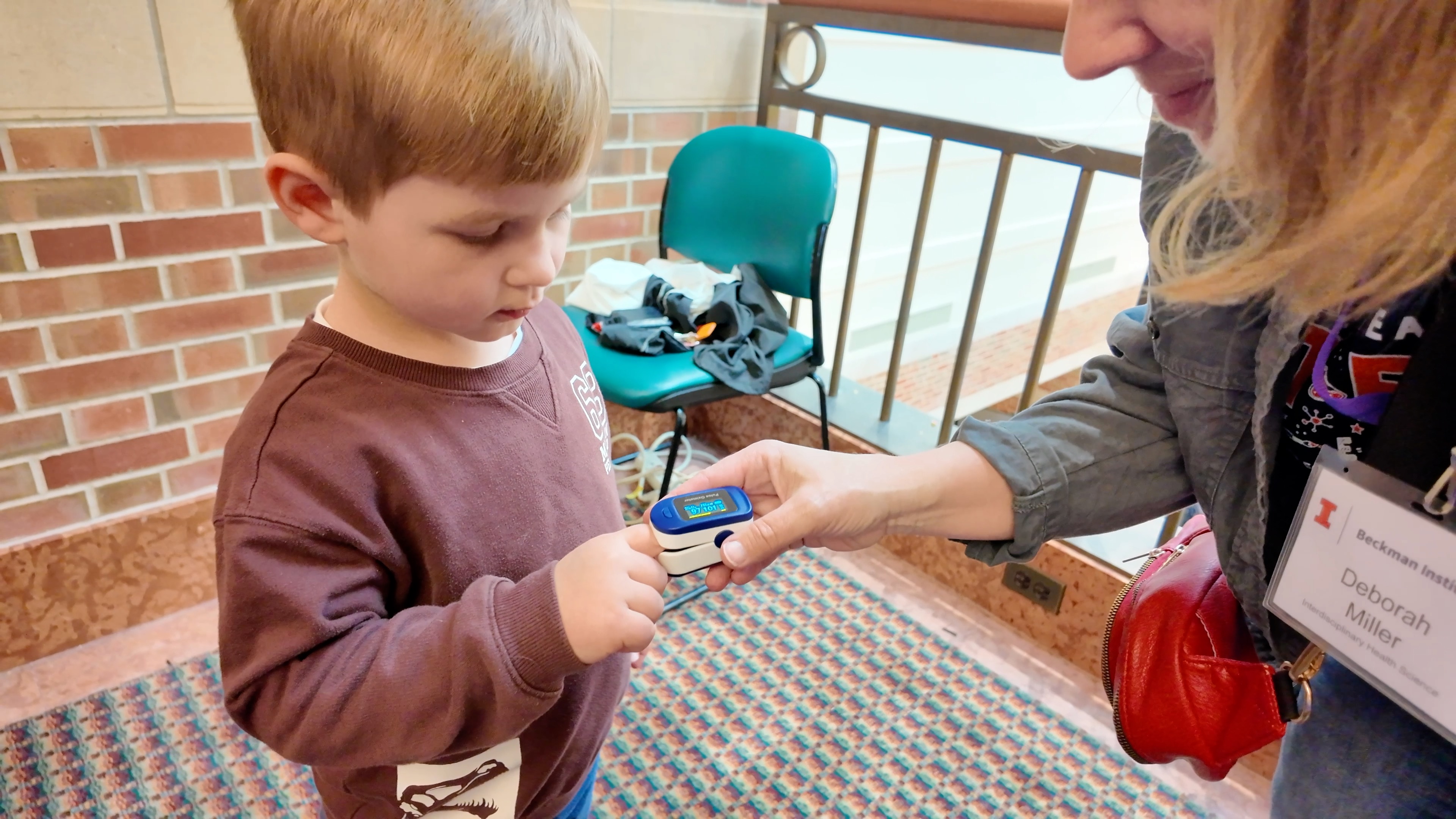 Close up of adult staff member helping young child measure pulse with an oximeter.