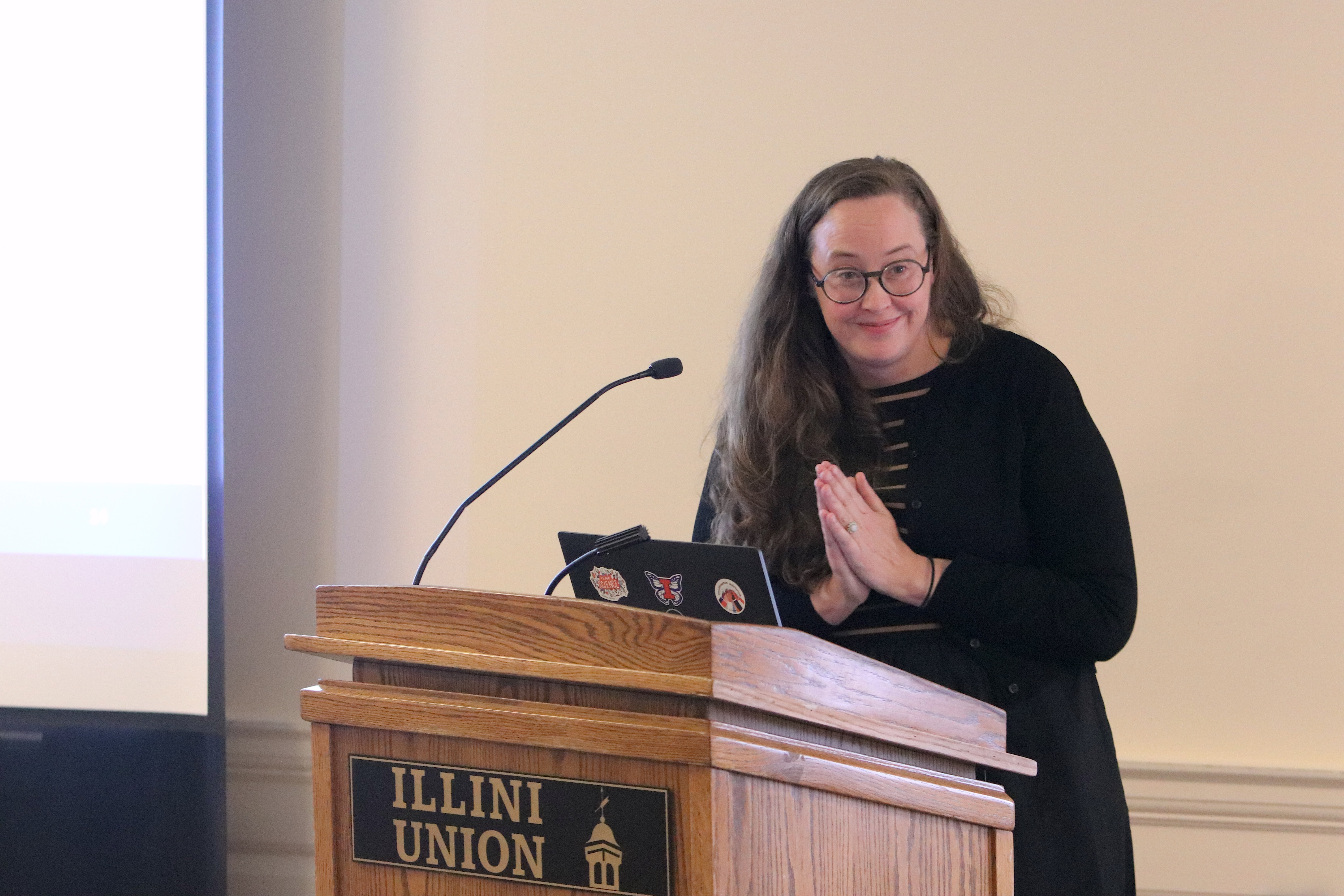 Catherine Corr, presenting from a lectern, gestures and smiles at an unseen audience.